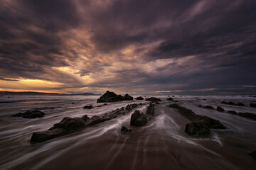Flysch of Barrika beach, Bizkaia, at sunset with a dramatic sky of warm colors and the tide water...