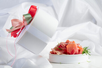 Prosciutto with rosemary in gift box on a white wooden table.