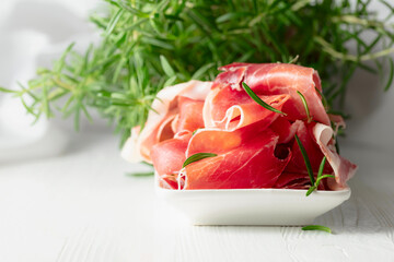 Prosciutto with rosemary on a white wooden table.