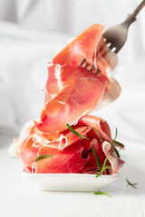 Prosciutto with rosemary on a white wooden table.