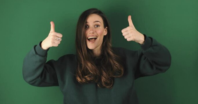 Young woman in green sweatshirt making good-bad sign isolated on green background. Girl make choice, or makes a decision thumb up or thumb down, like or dislike, yes or no. Girl diced thumbs up.