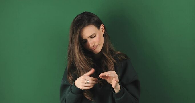 Depressed young woman looking at split brunette hair ends. Worried sad girl feels upset about brittle damaged dry hair loss concept. Female hormone problems concept isolated green background.