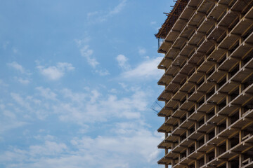 High-rise apartment building under construction against a blue sky with simple square reinforced...