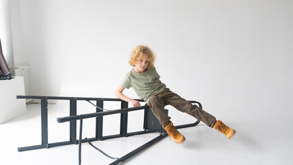 A young guy with curly hair poses sitting on a black metal staircase in a bright studio.