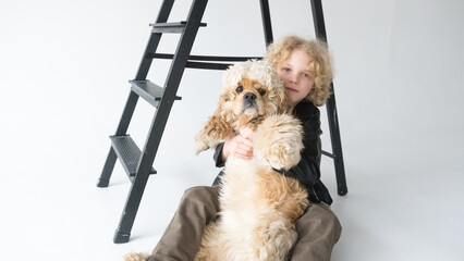 Young Boy Embracing His Fluffy Dog In Front of a Black Ladder on a White Background