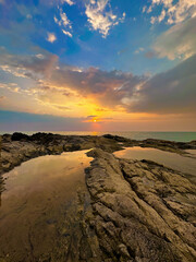 Warm sunset over tranquil beach with textured rocks and reflective tide pools, serene nature scene