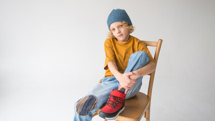 Child in electric blue jeans sits happily on a wooden chair with crossed legs