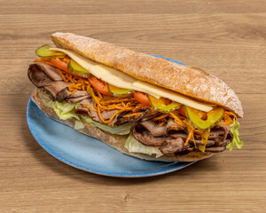 A roast beef submarine sandwich with cheese and tomatoes and pickle on a blue plate on a wooden table