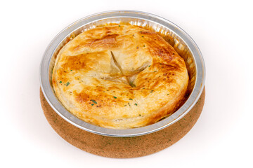 A baked savory meat pie in a foil tin on a cork trivet isolated on white