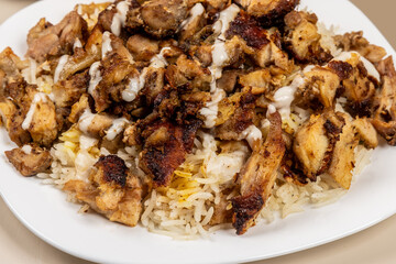 Chicken shawarma close up on a plate of rice with a drizzle of tahini or garlic sauce.