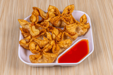A Chinese food appetizer, a bowl of deep fried stuffed wonton noodles with sweet red cherry sauce on a wooden table