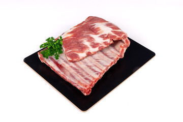 A raw, uncooked, rack of pork spare ribs with parsley garnish on a black plate isolated on white