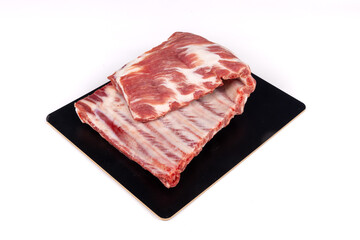 A raw, uncooked, rack of pork spare ribs folded over on a black plate isolated on white