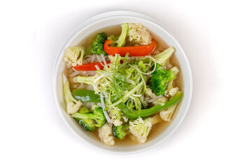 Overhead view of a white bowl of green vegetable Vietnamese Pho, soup on a white background