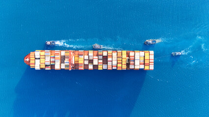 Top view Container ship full capacity approaching the port by a tugboat occupying the port International Container ship loading, unloading at sea port, Freight Transportation, Shipping,  