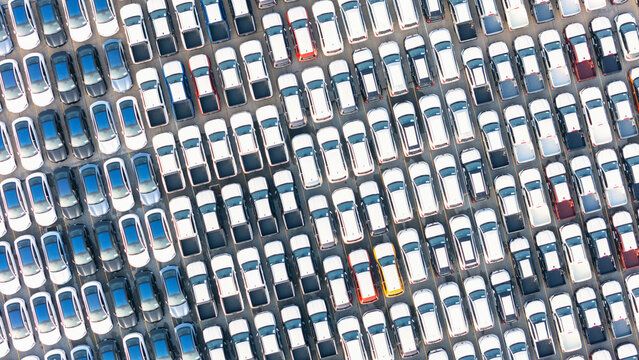 Top view of new cars stock at factory parking lot. Above view cars parked in a row. Automotive industry. Logistics business. Import or export new cars at warehouse. Big parking lot at port terminal