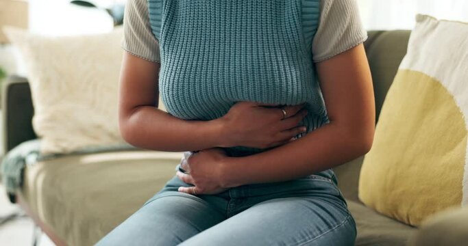 Woman, stomach ache and sick pain in home for menstruation, digestion or inflammation. Person, hands and bloated abdomen on sofa for uterus cramps with discomfort for tummy virus, ulcer or gut health