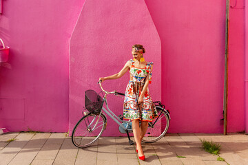 A beautiful girl with a bicycle near the facade of a pink house. Burano Island. Italy