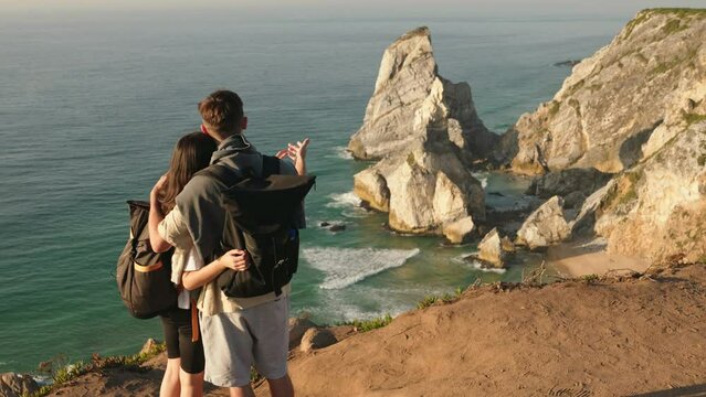 A couple with backpacks stands overlooking a stunning coast, capturing the essence of an adventure and the bond shared on a hike.