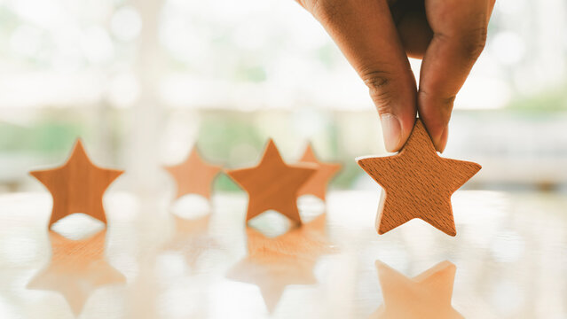 Businessman hand picking up model star on wooden table, Five star shape. The best excellent business services rating customer experience concept.