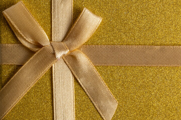 Gift box with ribbon bow on golden background. Top view.