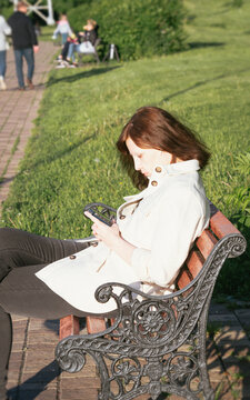 lone white jacket coat dressed brunette woman reading his smartphone on park bench