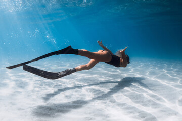 Freediver girl swimming underwater in blue sea over sandy sea bottom. Female training with fins...