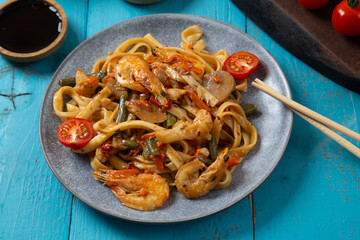 shrimp udon yaki soba sauce on a blue table next to cherry tomatoes soy sauce and chopsticks