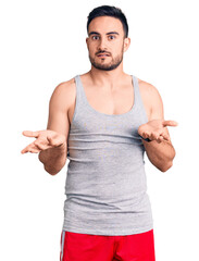 Young handsome man wearing swimwear and sleeveless t-shirt clueless and confused with open arms, no...