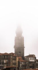 Church of the Clerics, baroque from the 17th century, standing out among the houses and roofs of the historic neighborhood of Porto, covered by fog and rain clouds on a romantic and bucolic gray day.