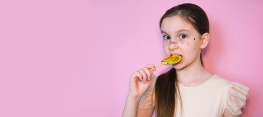 Banner. Portrait of happy smiling little girl with lollipop. Sugar for children. Little sweet tooth on pink background. Girl with bright makeup. Glittery glitter on face.