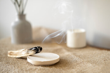 Palo santo stick emitting smoke near a candle on a table, warmth of home and tranquility