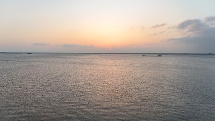 Serene sunset over a calm sea with distant boats and a pastel sky, ideal for backgrounds and...