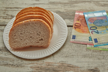 Bread on a plate on the table next to euro bills of different denominations, sale of bread in Europe, rising food prices in Europe - obrazy, fototapety, plakaty