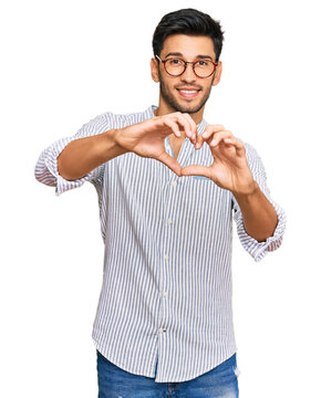 Young handsome man wearing casual clothes and glasses smiling in love doing heart symbol shape with hands. romantic concept.