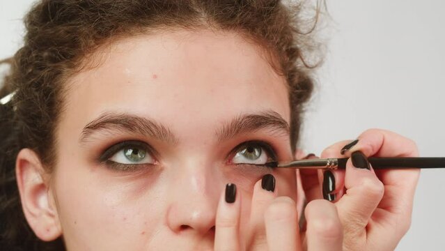 Eye shadow makeup to the upper eyelid, close-up. Makeup artist applies a bright eye shadow with a make-up brush.Tutorial master class of professional makeup, smoky eyes 