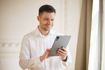 An affable businessman in a white shirt confidently utilizes a tablet, his engagement with the device reflecting a blend of technology and ease.