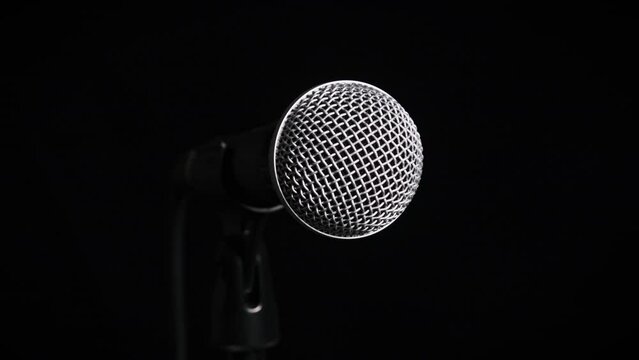 The vocal microphone slowly rotates on a black background close-up. Chrome grid on dynamic mic surface slowly turning. Concept recording studio, voice, podcast, karaoke, audiobook. Copy space