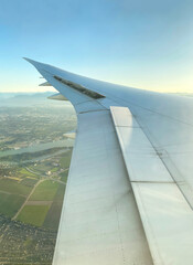 View from airplane window. Wing of an aircraft. Aerial view of a city with green land and...