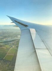 View from airplane window. Wing of an aircraft. Aerial view of a city with green land and mountains. The white wing of the plane with the earth below.
