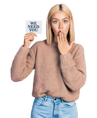 Beautiful young blonde woman holding we need a change banner covering mouth with hand, shocked and...