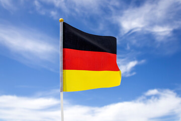 Flag of Germany fluttering in the wind in front of blue sky with white clouds