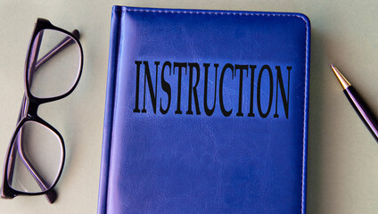 INSTRUCTION - word on blue notebook on grey background with pen and glasses
