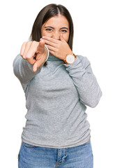 Young beautiful woman wearing casual turtleneck sweater laughing at you, pointing finger to the camera with hand over mouth, shame expression