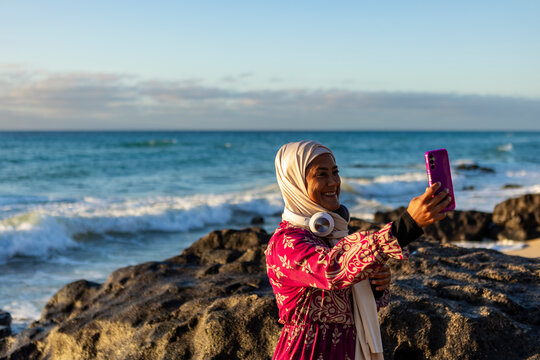Joyful Muslim Woman Taking Selfie at Seaside