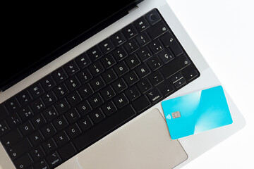 Top view of sleek laptop keyboard with a bright blue contactless payment card placed on its trackpad, depicting modern payment methods and online shopping