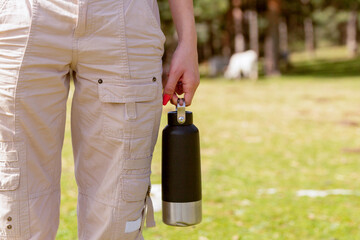 Captured in nature, anonymous woman enjoys a sunny getaway, holding a practical and reusable water bottle, ready for a day of adventure outdoors