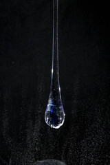 Gota de vidro azul semi transparente em fundo preto. Fotografia em close up de uma peça similar a...