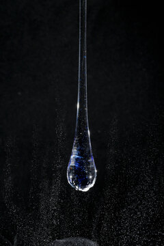Gota de vidro azul semi transparente em fundo preto. Fotografia em close up de uma peça similar a um líquido de alta viscosidade pingando em cima de glitter branco.