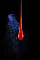 Gota de vidro vermelho semi transparente em fundo preto com glitter azul. Fotografia em close up de uma peça similar a um líquido de alta viscosidade pingando. - obrazy, fototapety, plakaty